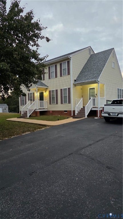 Two-story exterior featuring light-colored siding, dark shutters, an asphalt shingled roof, dual elevated entryways with white railing, and a paved driveway