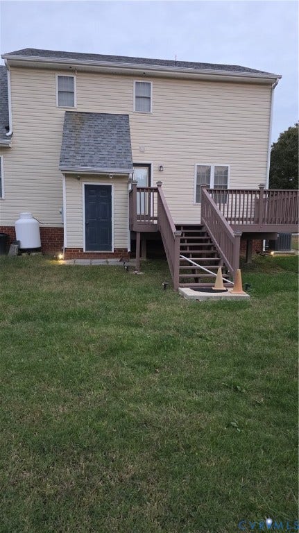 Rear exterior featuring light-colored horizontal siding, a raised wooden deck with staircase, brick foundation accents, and an open backyard