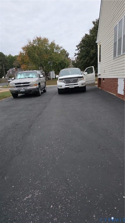 Asphalt driveway with red brick foundation detailing and horizontal siding