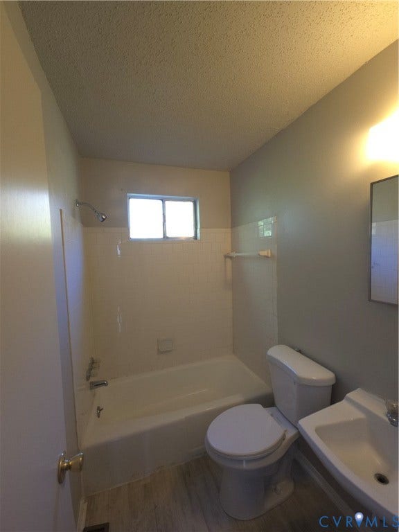 413 Adamson Street, Henrico, VA 23075 Bathroom featuring a porcelain tub with tile surround, wall-mounted shower head, ceramic sink with chrome hardware, and wood-finish flooring