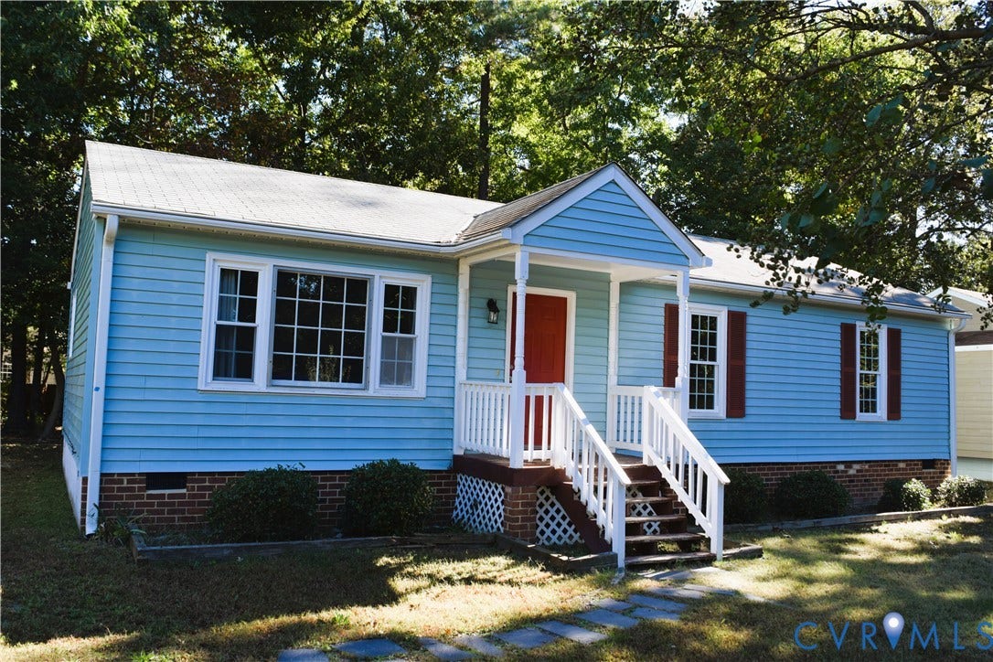 8905 Hawkbill Road, Chesterfield, VA 23237 Single-story exterior featuring light blue horizontal siding, red shutters, a gable-roofed front porch, white railings, and brick foundation masonry
