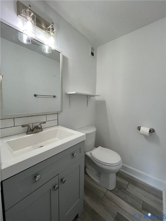 39 Rock Garden Lane, Henrico, VA 23228 Grey vanity with integrated rectangular sink, wood-finish flooring, subway tile backsplash, wall-mounted shelving, and dual-light vanity fixture