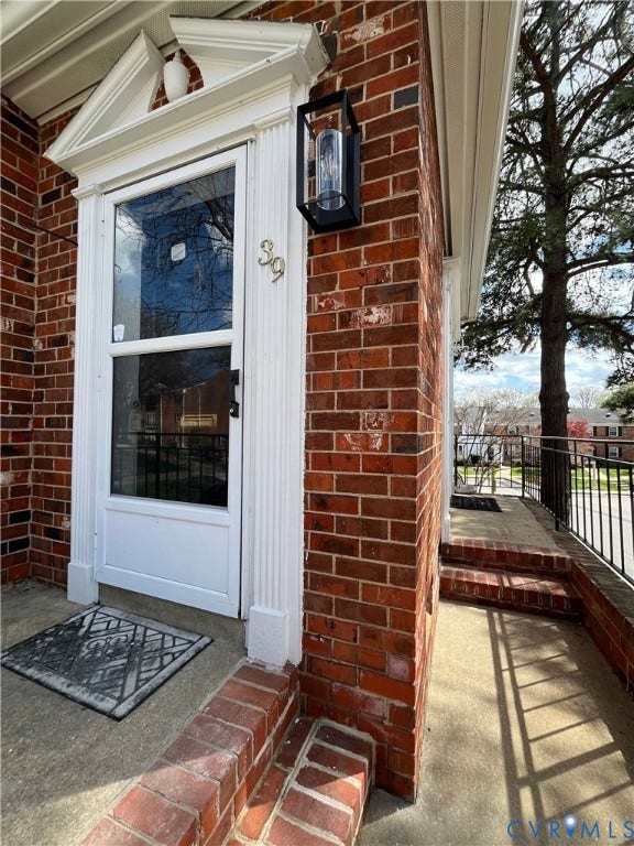 39 Rock Garden Lane, Henrico, VA 23228 Red brick exterior featuring a white pilaster-framed entryway with a pediment, concrete steps with brick edging, and a black metal exterior sconce