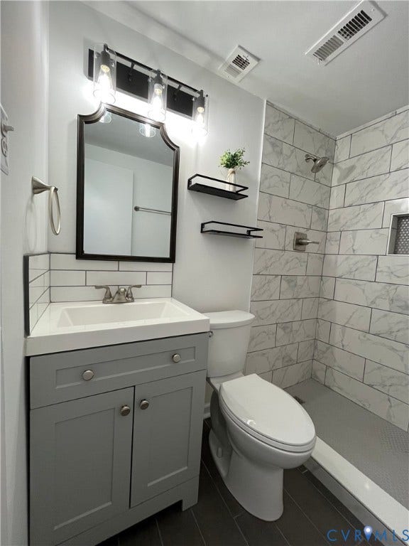 39 Rock Garden Lane, Henrico, VA 23228 Bathroom featuring a grey vanity with a rectangular sink, stone-finish shower surround with recessed shelving, dark tile flooring, and a framed vanity mirror with three-light fixture