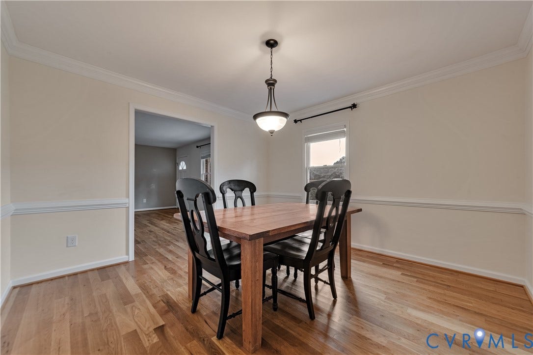 Dining area featuring wood-finish flooring, crown molding, chair rail trim, and a decorative pendant light fixture