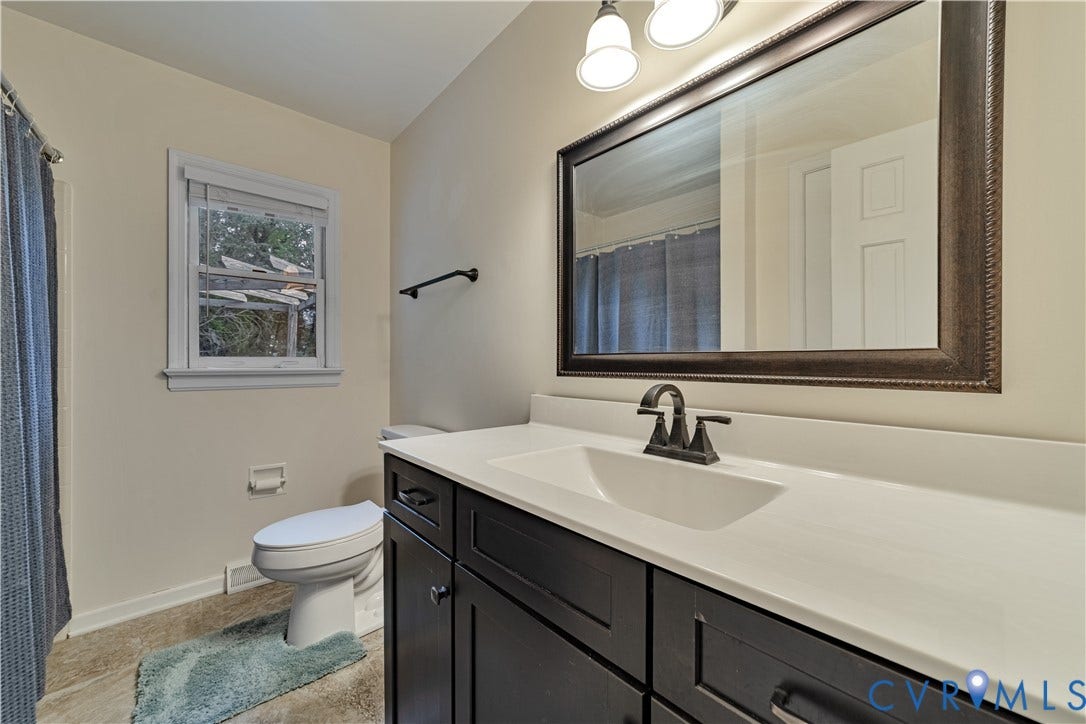 Dark wood-finish vanity with a white countertop, integrated sink, oil-rubbed bronze faucet, and a wall-mounted framed mirror