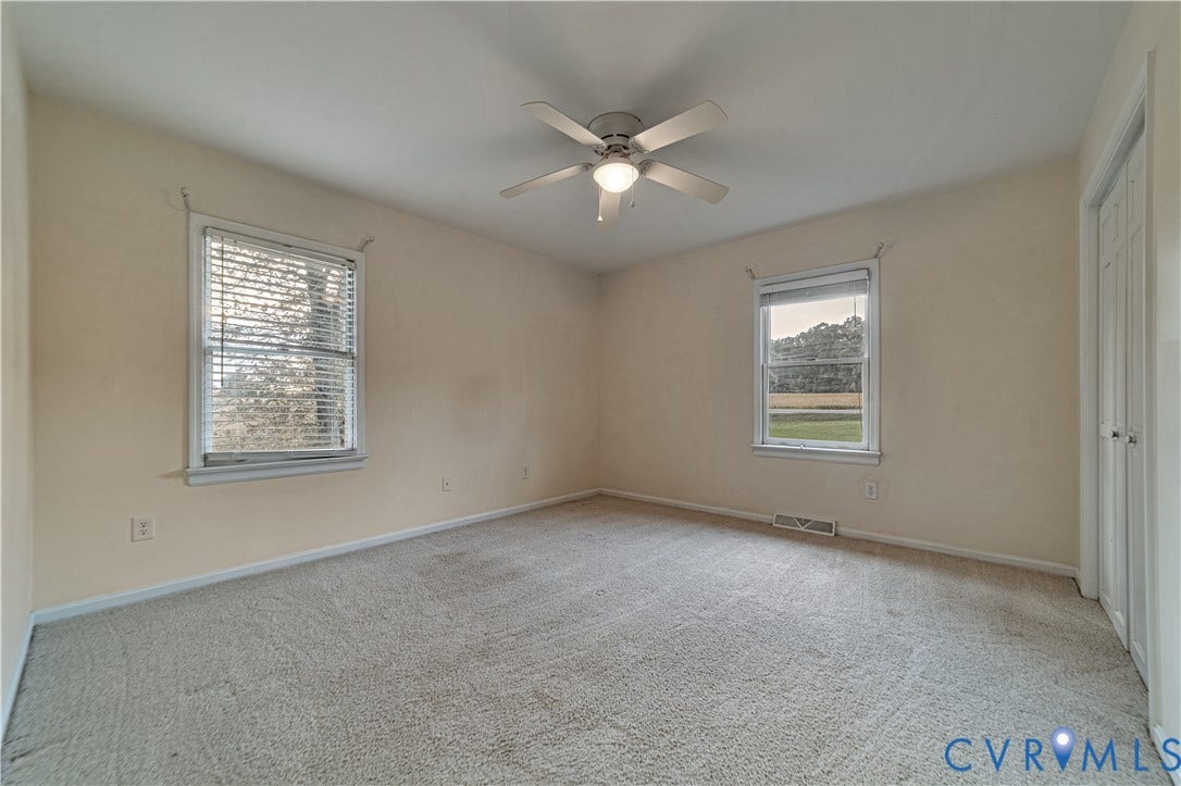 Neutral-toned interior featuring wall-to-wall carpeting, two double-hung windows, and a central ceiling fan with an integrated light fixture