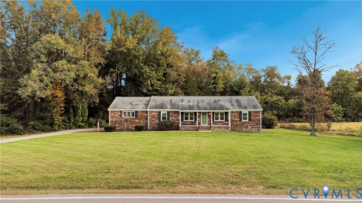 Single-story brick exterior featuring a shingled roof, multi-pane windows, and a sprawling front lawn set against a backdrop of mature trees