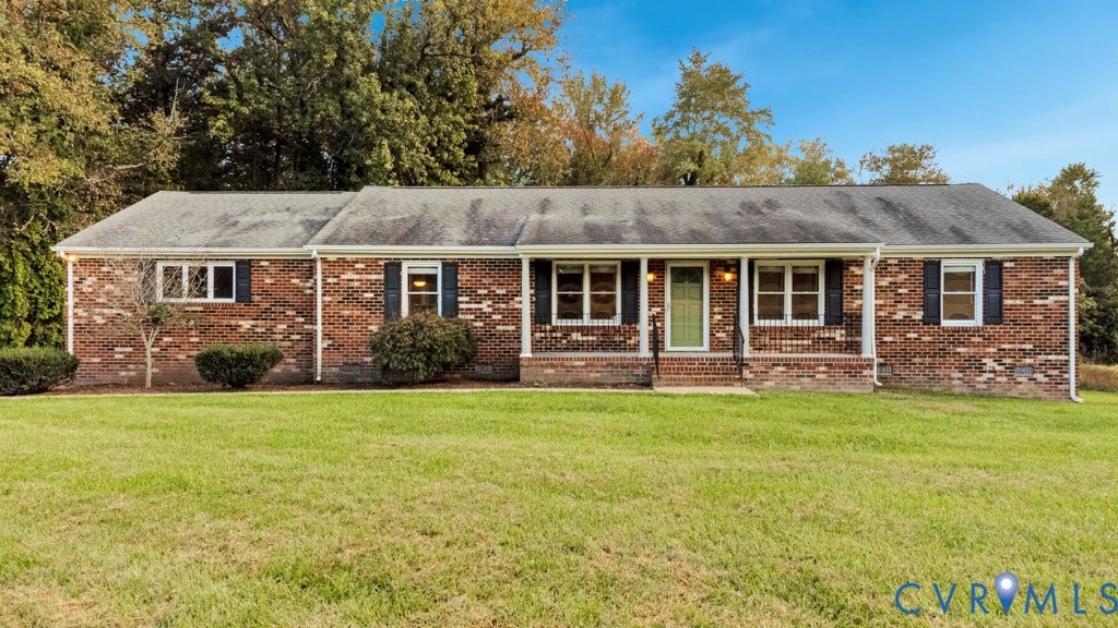 Single-story brick exterior featuring a covered front porch, wrought iron railings, multi-pane windows with shutters, and expansive lawn frontage