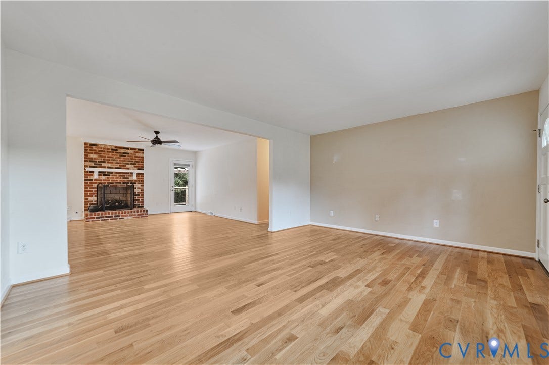 Living area featuring light wood-finish flooring, masonry fireplace with a white mantel, ceiling fan, and entry door with glass paneling