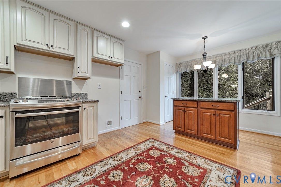Kitchen featuring light-toned cabinetry, stainless steel gas range, stone-surface countertops, wood-finish flooring, and a free-standing wooden island