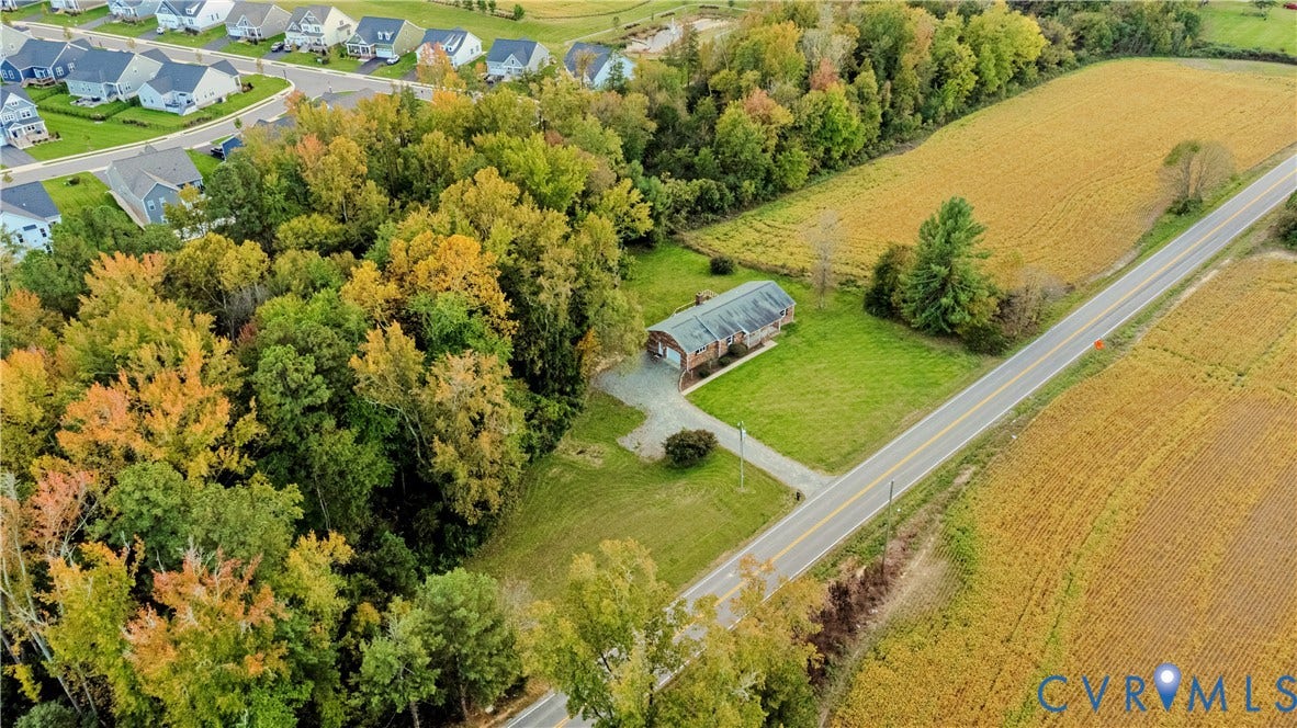 Aerial perspective of property featuring extensive wooded acreage, open lawn space, a single-story dwelling, and an asphalt driveway