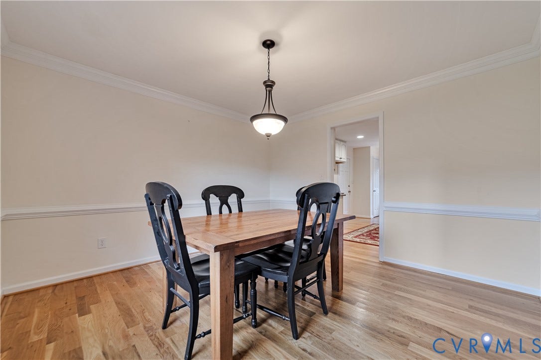 Room featuring wood-finish flooring, chair rail molding, crown molding, and a suspended metal pendant light fixture