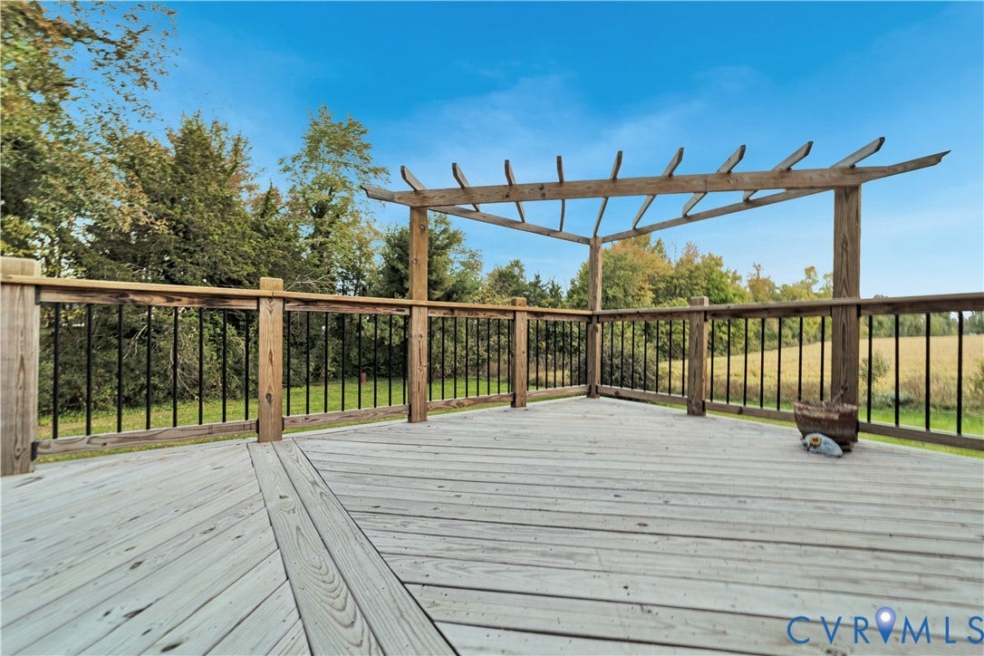 Elevated wood deck featuring a wooden pergola, diagonal plank flooring, and a railing with vertical metal balusters
