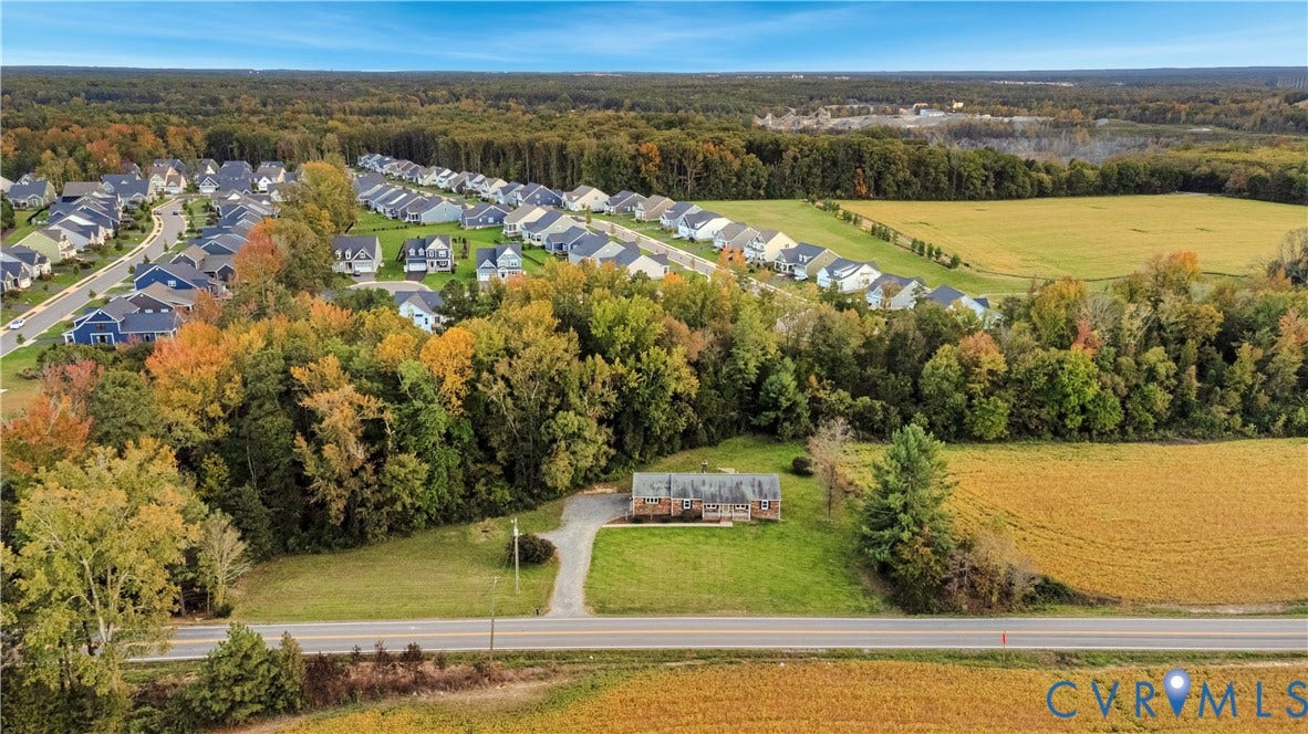 Aerial perspective featuring a detached residential structure, a paved driveway, and expansive acreage bordered by mature trees and open fields
