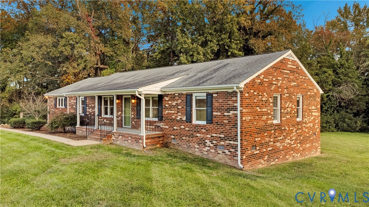Single-story brick exterior featuring a covered front porch, dark shutter accents, and a wide grassy lawn