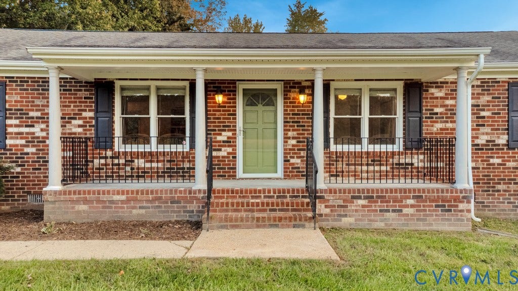 Brick exterior featuring a covered front porch with round columns, black wrought iron railing, and a central entryway