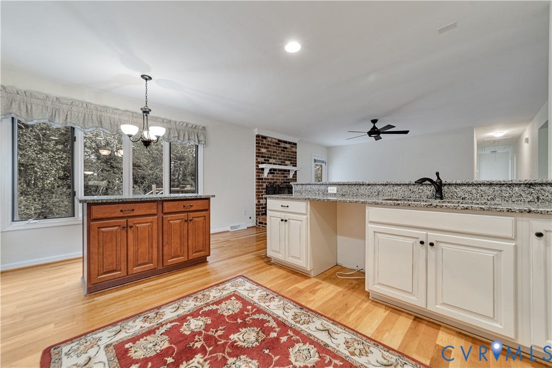 Kitchen featuring wood-finish flooring, white cabinetry, a freestanding wood-finish island, stone-finish countertops, and a brick fireplace