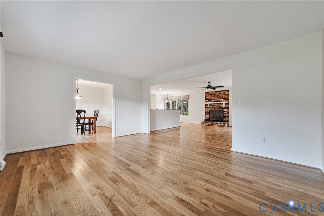 Open-concept interior featuring wood-finish flooring, a full-height brick masonry fireplace with a white mantel, and ceiling-mounted fans