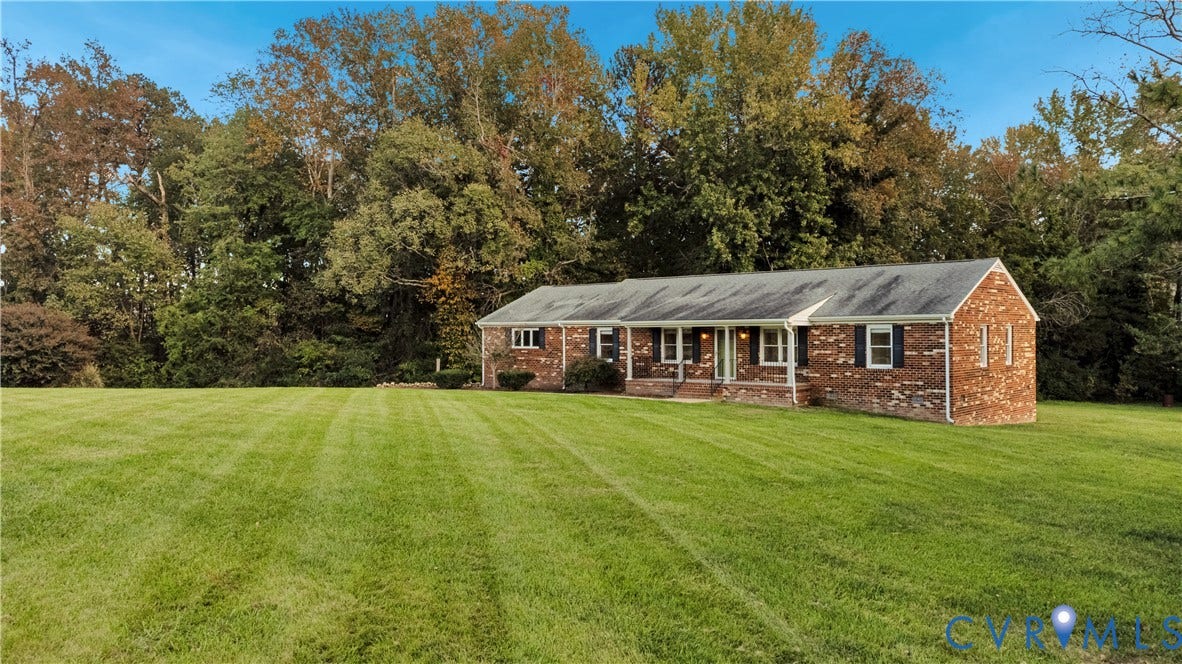 Single-story brick exterior featuring a shingled gable roof, shutters, and an expansive lawn set against a backdrop of mature trees