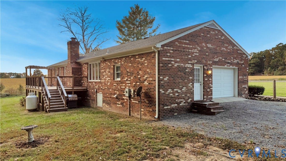 Brick exterior residence featuring an elevated wood deck, attached single-car garage, and gravel driveway