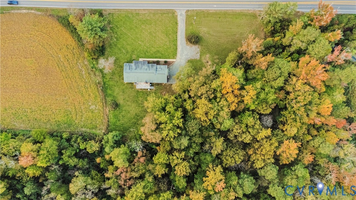 Aerial perspective of a detached residence featuring a gravel driveway, expansive grass acreage, and mature tree borders
