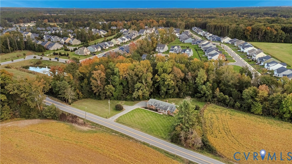 Aerial perspective of a property featuring a detached residence, expansive grass lawn, paved driveway, and mature perimeter trees
