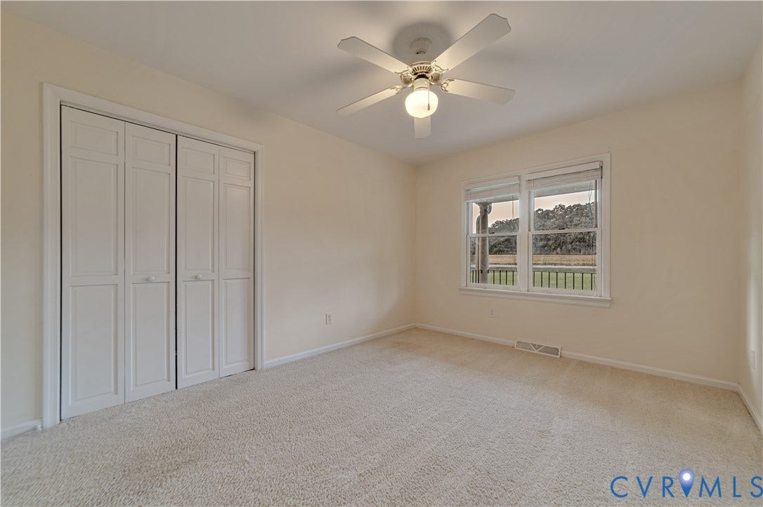 Neutral-toned interior room featuring wall-to-wall carpeting, white bi-fold closet doors, a white ceiling fan with integrated lighting, and dual-pane windows
