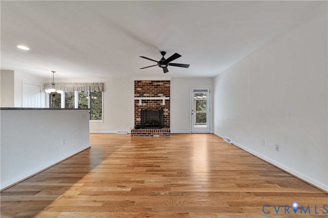 Living area featuring wood-finish flooring, a brick fireplace with a mantel, a ceiling fan, and a glass-paneled exterior door