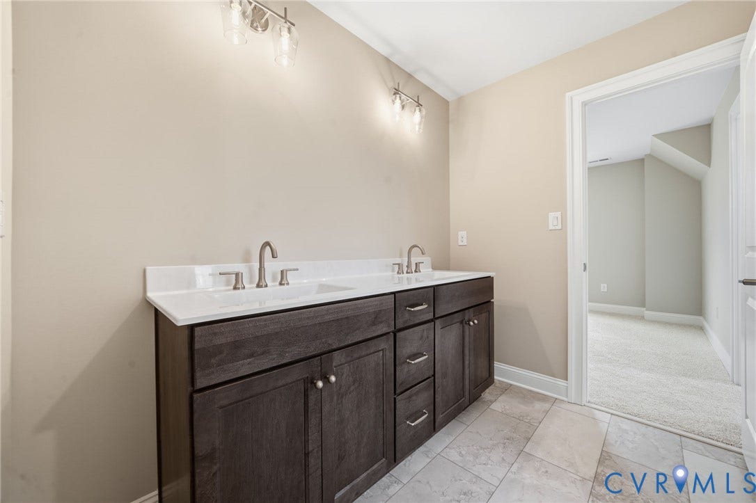 18132 Dogwood Trail Way, Rockville, VA 23146 Dual-sink vanity with dark wood-finish cabinetry, solid surface countertop, metallic hardware, and wall-mounted light fixtures, complemented by tile flooring