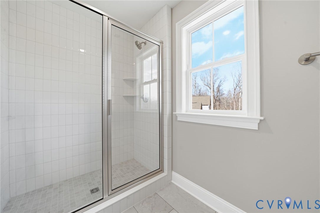 18132 Dogwood Trail Way, Rockville, VA 23146 Walk-in shower featuring white tiled walls, a metal-framed glass enclosure, built-in shelving, and a dual-pane window