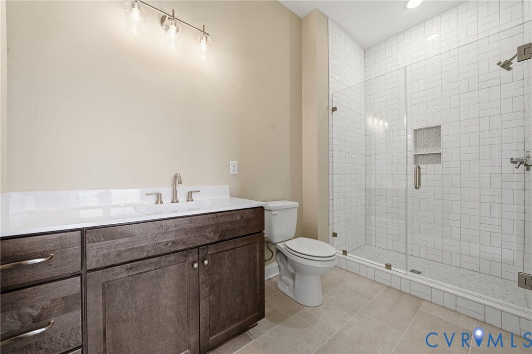 18132 Dogwood Trail Way, Rockville, VA 23146 Dark-finish wood vanity with a white countertop, integrated sink, wall-mounted light fixture, and a glass-enclosed shower featuring white subway-style tile and an integrated niche