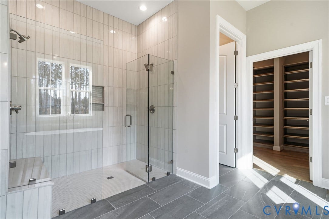 18132 Dogwood Trail Way, Rockville, VA 23146 Walk-in shower featuring floor-to-ceiling vertical tile surround, glass enclosure, built-in tiled bench, and rainfall showerhead, complemented by large-format slate-finish floor tile and walk-in closet with built-in shelving