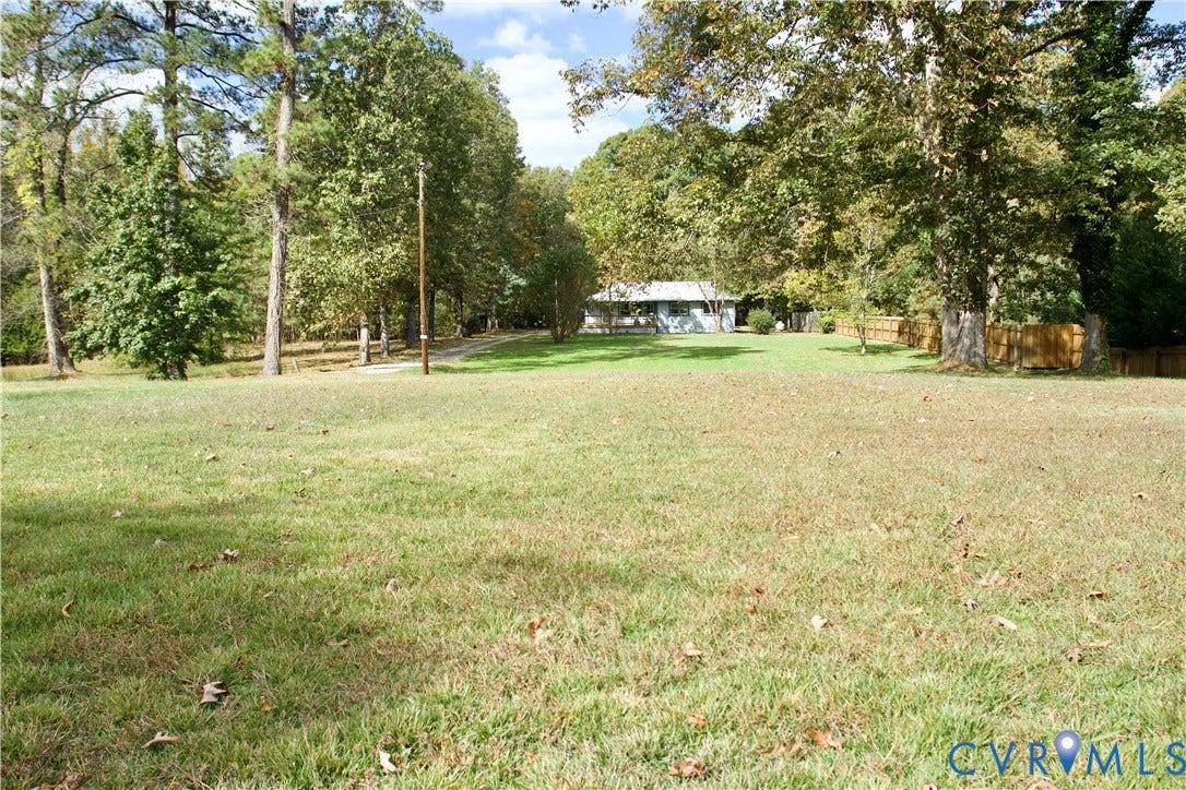 9012 Shawonodasee Road, Courthouse, Chesterfield, VA 23832 Expansive grassy lot featuring mature tree canopy, wood-panel fencing, and a gravel driveway