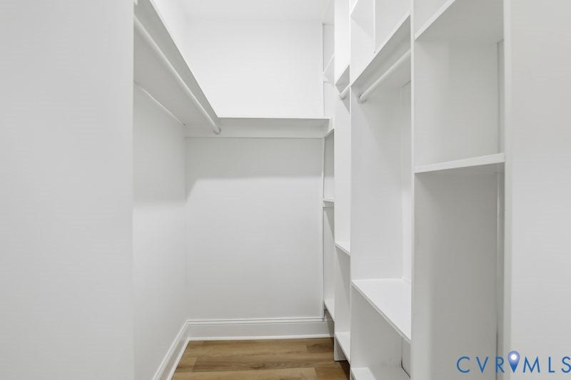 Customized walk-in closet featuring floor-to-ceiling built-in white shelving, integrated hanging rods, and wood-finish flooring