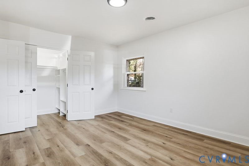 Neutral interior featuring wood-finish flooring, a single window, and a closet with double-panel doors and built-in shelving