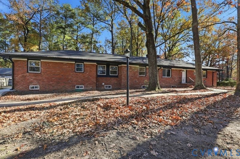 Single-story brick exterior featuring a low-pitch roof, dark trim, grid-style windows, and a paved walkway