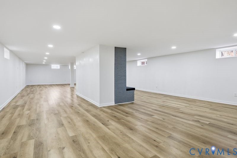 Open-concept area featuring wood-finish flooring, recessed lighting, and a prominent floor-to-ceiling brick pillar with an integrated hearth
