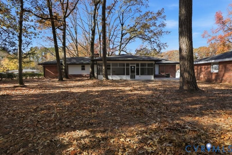 Exterior of a brick-clad home featuring a screened-in porch and mature trees on a wooded lot