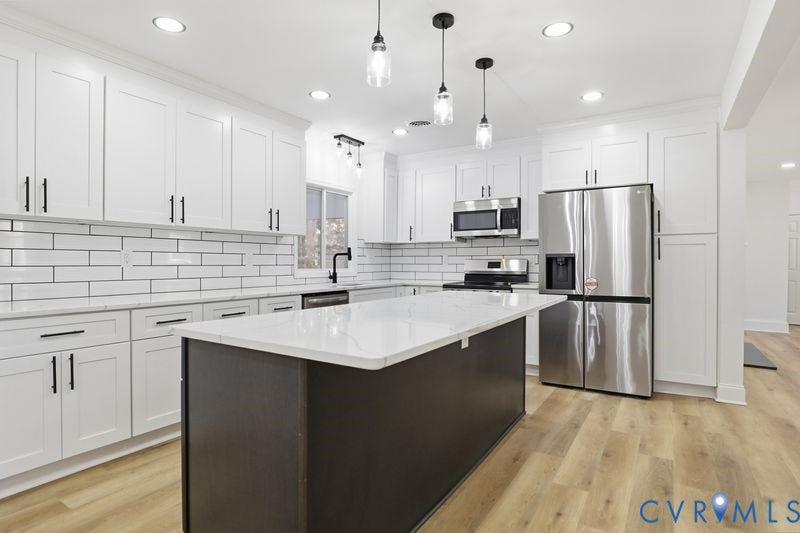 Kitchen featuring white shaker-style cabinetry, an expansive center island with a stone-finish countertop, subway tile backsplash, stainless steel appliances, and wood-finish flooring