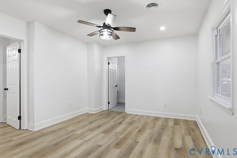 Room featuring wood-finish flooring, a multi-blade ceiling fan with integrated lighting, recessed ceiling lights, and two six-panel interior doors