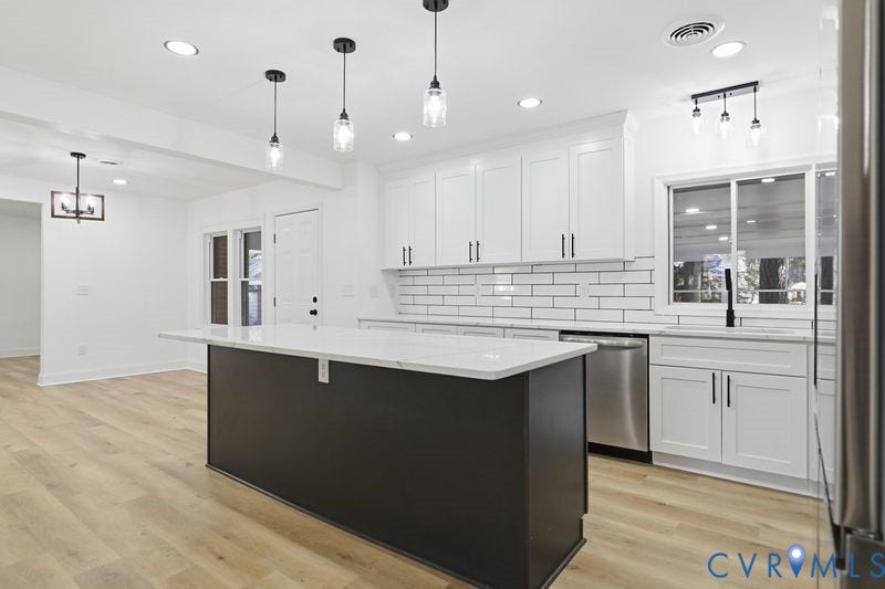 Kitchen featuring a central island with a solid surface countertop, white shaker-style cabinetry, subway tile backsplash with dark grout, wood-finish flooring, and pendant lighting