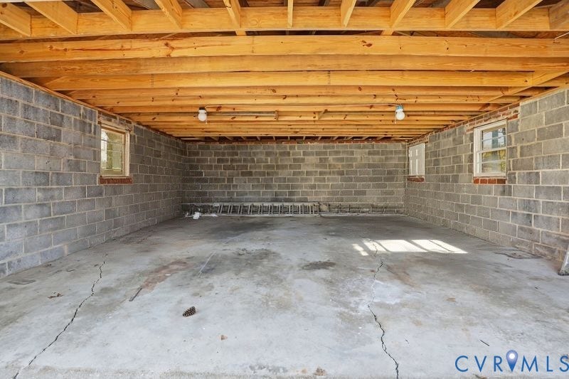 Unfinished lower-level space featuring exposed timber joist ceiling, concrete block walls, and concrete flooring, punctuated by multiple inset windows