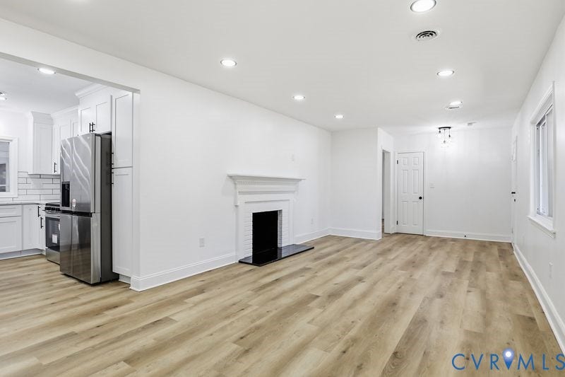 Open-concept interior featuring wood-finish flooring, recessed lighting, and a white fireplace mantel with a black hearth