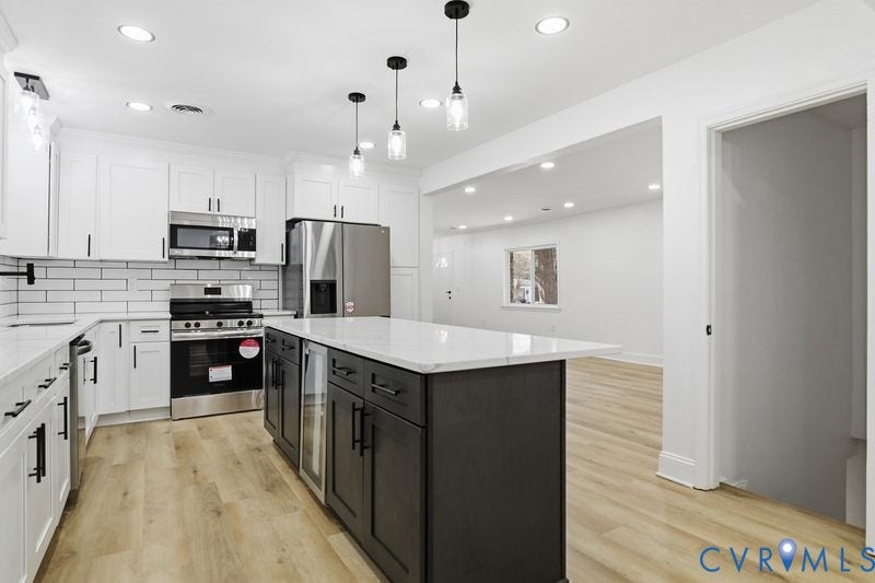 Kitchen featuring white shaker cabinetry, an oversized center island with a stone-finish countertop, stainless steel appliances, a white subway tile backsplash, and wood-finish flooring