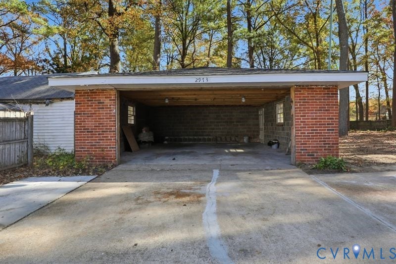 Covered carport featuring a concrete driveway, brick exterior pillars, and exposed wood ceiling joists