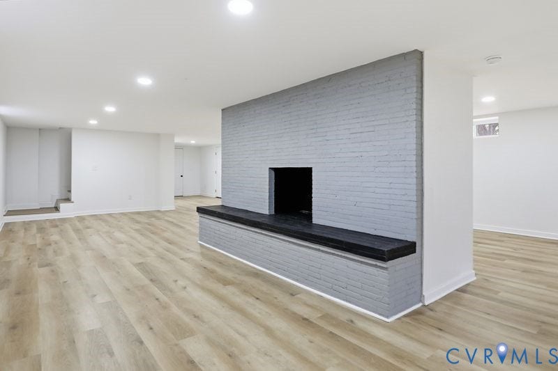 Open-concept interior featuring wood-finish flooring, recessed lighting, and a prominent gray brick fireplace with a built-in hearth