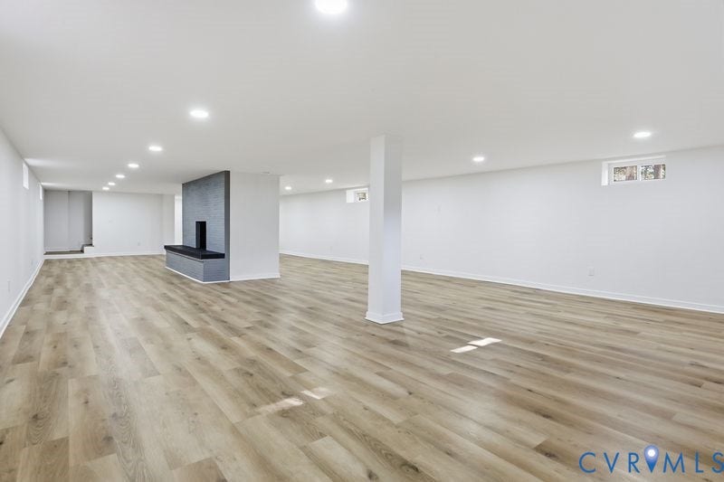 Open-concept interior featuring wood-finish flooring, recessed lighting, and a prominent center fireplace with a dark brick surround and built-in hearth