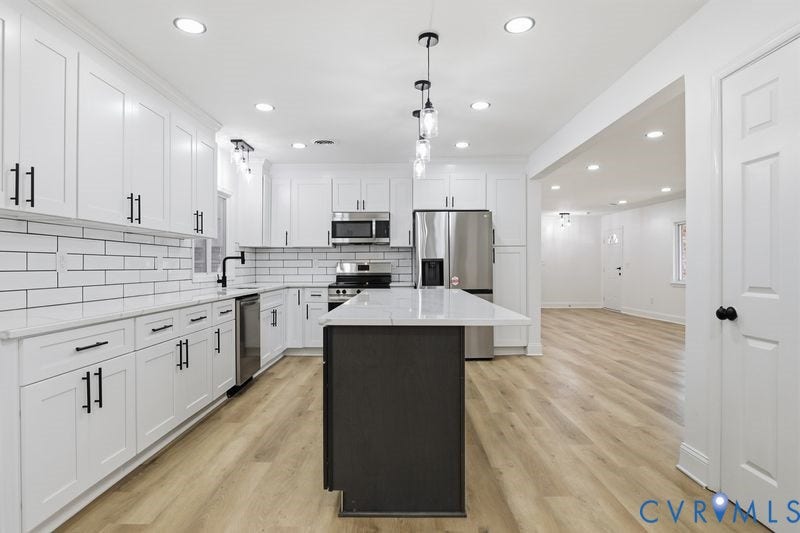 Kitchen featuring white shaker-style cabinetry, a central island with a contrasting dark base, stone-surface countertops, a subway tile backsplash, and stainless steel appliances