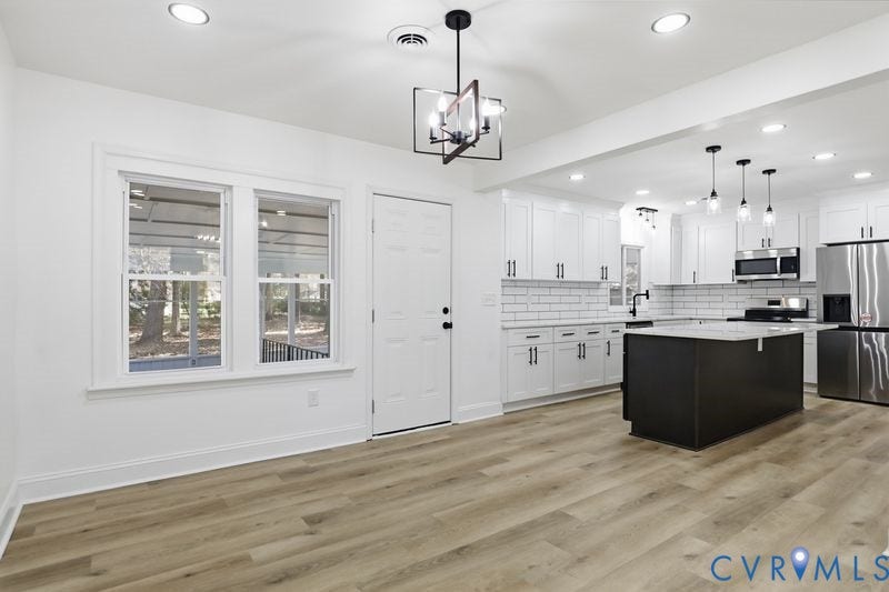 Open kitchen featuring a center island with a stone countertop, white cabinetry, subway tile backsplash, stainless steel appliances, and wood-finish flooring
